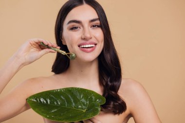 Mükemmel ciltli güzel bir kadının yarı çıplak portresini kapat. Bej arka planda doğal kuvars taşıyla yüz masajı yap..