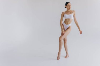 İnce vücutlu, beyaz stüdyo arka planında fotokopi aletiyle poz veren güzel bir kadının tam boy portresi.