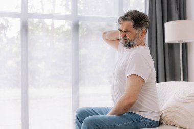 Üst sınıflardan biri içeride oturuyor, boynu ağrıyormuş gibi görünüyor. Üzüntülü bir ifadeyle boynunu tutuyor, rahatsız olduğunu gösteriyor..