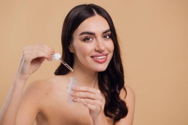 Bej arka planda Serum Bırakan Kadın. Pipette 'ten Serum Kolajeni Nemlendirici kullanan Avrupalı Kız. Yakın plan. Pozitif Gülen Güzel Kadın Portresi. Yüz Cildi Bakımı Konsepti