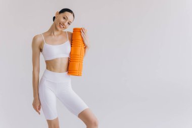 Beyaz spor giysili güzel, ince kadın spor kıyafetleri içinde, spor salonu için turuncu köpük silindirli, fotokopi alanlı beyaz poz veren, sağlığını ve sağlığını destekleyen,.