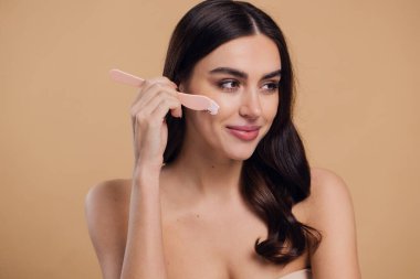 Yarı çıplak kadın, güzellik için yüz ve fırça kremi, kuaför ve cilt bakımı bej arka planda. Mutlu model, yüz losyonu ve dermatoloji, kolajen ve mutluluğun gülümsemesi için makyaj malzemesi.