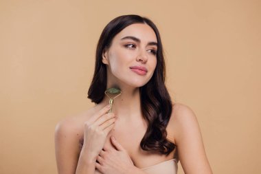 Mükemmel ciltli güzel bir kadının yarı çıplak portresini kapat. Bej arka planda doğal kuvars taşıyla yüz masajı yap..