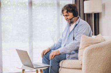 Dedem dizüstü bilgisayar ve kulaklık kullanıyormuş. Koltukta oturuyormuş. Evden çalışan kıdemli adam, çevrimiçi toplantı, görüntülü konuşma, kopyalama alanı
