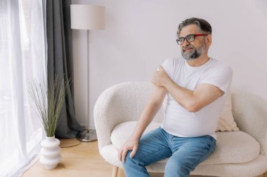 Artrit belirtileri. Evde omuz ağrısı çeken yaşlı sakallı adam.