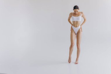 İnce vücutlu, beyaz stüdyo arka planında fotokopi aletiyle poz veren güzel bir kadının tam boy portresi.