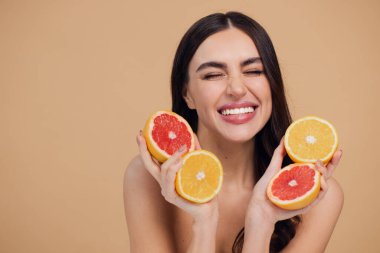 Genç bir kadının portresi, portakal rengi greyfurt gülümseyen dişlerin yarısını beslenen vejetaryen vitamin yaz vitamini, saç bakımı, doğal organik vegan narenciye bej arka planda.