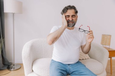 Home, senior man and headache on sofa for stress, emotional conflict and temporal vertigo. Living room, couch and old person with pain, migraine and anxiety due overthinking in retirement in house clipart