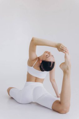 Zayıf vücutlu sporcu bir kadının beyaz arka planda izole edilmiş yoga pratiği yaparken tam boy görüntüsü. Vücut ve zihinsel gelişim arasındaki sağlıklı yaşam ve doğal denge kavramı.