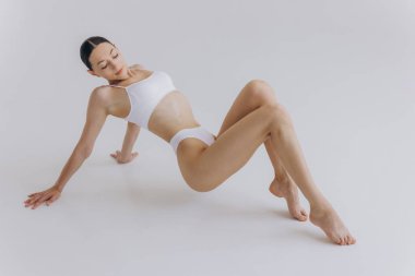 Formda ve güzel bir kadın ve mükemmel bir fiziği var. Yerde beyaz iç çamaşırlı bir kız var. Sağlıklı yaşam tarzı, spor, sağlık, beslenme ve diyet konsepti