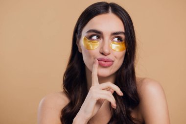 Saf, güzel, kibar bir kadının güzel görüntüsü. Çıplak, soyutlanmış bir kamera gibi duruyor. Bej arka planda altın rengi bantlarla cildine dikkat et.