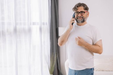 Yakışıklı, sakallı, son sınıf öğrencisi cep telefonuyla konuşurken pencereden dışarı bakıyor. Yaşlı erkek kahkahalar atıyor