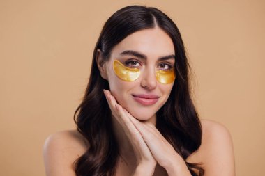 Saf, güzel, kibar bir kadının güzel görüntüsü. Çıplak, soyutlanmış bir kamera gibi duruyor. Bej arka planda altın rengi bantlarla cildine dikkat et.