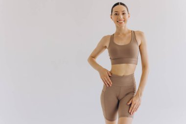 Beyaz arka planda bej renkli spor giysili zayıf bir kadın izole edilmiş. Düz göbekli, kaslı, zayıf, çekici bir kadın. Uzayı metin için kopyala. Vücut bakımı, sağlıklı ve sportif yaşam, saç aldırma, yoga konsepti
