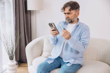 Yaşlı bir adam kanepede tek başına oturuyor. Bir hasta gözlük takıyor. Akıllı telefondan talimatları okuyor.