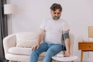 Evdeki kanepede oturmuş, tansiyonunu ölçen, gri saçlı, son sınıf öğrencisi. Modern tonometre kullanan emekli, hipertansiyon deneyimi yaşayan, kopyalama alanı