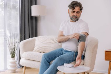 Evdeki kanepede oturmuş, tansiyonunu ölçen, gri saçlı, son sınıf öğrencisi. Modern tonometre kullanan emekli, hipertansiyon deneyimi yaşayan, kopyalama alanı