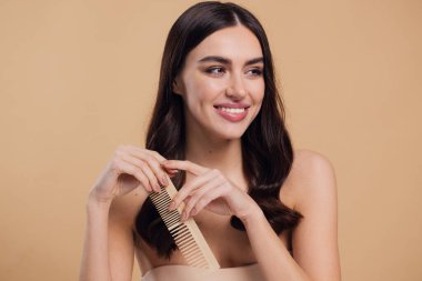 Çıplak omuzlarını bayanla su kuyusu-damat rüya gibi esmer saç o ahşap fırça pastel bej renkli arka plan üzerinde izole ile saç tarama büyüleyici portre yapmak beyaz ışınlama dişleri kazma dişli bir gülümseme