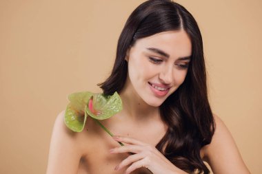 Bej renkli stüdyo arka planında izole edilmiş çiçekle poz veren çekici genç bir kadının güzel portresi.