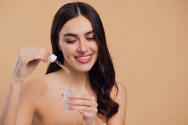 Bej arka planda Serum Bırakan Kadın. Pipette 'ten Serum Kolajeni Nemlendirici kullanan Avrupalı Kız. Yakın plan. Pozitif Gülen Güzel Kadın Portresi. Yüz Cildi Bakımı Konsepti