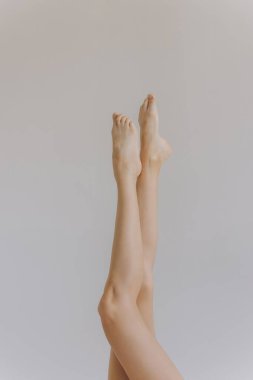 Bacak bacak üstüne atan genç bir kadın beyaz arka planda pürüzsüz bir ten gösteriyor. Kız güzellik modeli vücut bakım losyonu, epilasyon, tüy dökümü, ağda, pedikür, şekerleme..