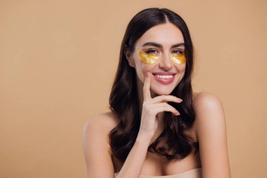 Saf, güzel, kibar bir kadının güzel görüntüsü. Çıplak, soyutlanmış bir kamera gibi duruyor. Bej arka planda altın rengi bantlarla cildine dikkat et.