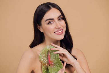 Bej renkli stüdyo arka planında izole edilmiş çiçekle poz veren çekici genç bir kadının güzel portresi.