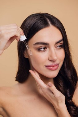 Bej arka planda Serum Bırakan Kadın. Pipette 'ten Serum Kolajeni Nemlendirici kullanan Avrupalı Kız. Yakın plan. Pozitif Gülen Güzel Kadın Portresi. Yüz Cildi Bakımı Konsepti
