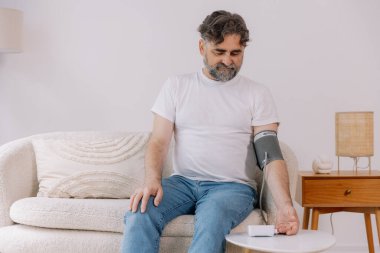 Evdeki kanepede oturmuş, tansiyonunu ölçen, gri saçlı, son sınıf öğrencisi. Modern tonometre kullanan emekli, hipertansiyon deneyimi yaşayan, kopyalama alanı
