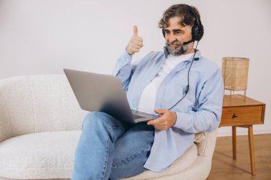 Dedem dizüstü bilgisayar ve kulaklık kullanıyormuş. Koltukta oturuyormuş. Evden çalışan kıdemli adam, çevrimiçi toplantı, görüntülü konuşma, kopyalama alanı