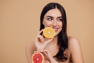Genç bir kadının portresi, portakal rengi greyfurt gülümseyen dişlerin yarısını beslenen vejetaryen vitamin yaz vitamini, saç bakımı, doğal organik vegan narenciye bej arka planda.