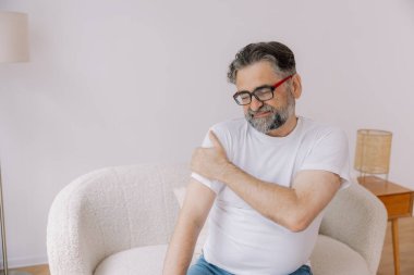 Artrit belirtileri. Evde omuz ağrısı çeken yaşlı sakallı adam.
