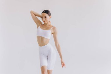 Beyaz arka planda beyaz spor giyimli zayıf bir kadın izole edilmiş. Düz göbekli, kaslı, zayıf, çekici bir kadın. Uzayı metin için kopyala. Vücut bakımı, sağlıklı ve sportif yaşam, saç aldırma, yoga konsepti