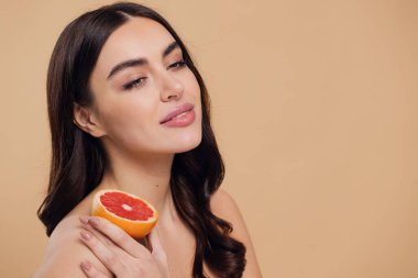 Genç bir kadının portresi, portakal rengi greyfurt gülümseyen dişlerin yarısını beslenen vejetaryen vitamin yaz vitamini, saç bakımı, doğal organik vegan narenciye bej arka planda.