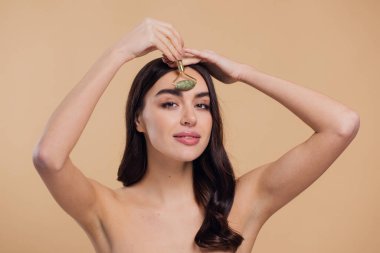 Mükemmel ciltli güzel bir kadının yarı çıplak portresini kapat. Bej arka planda doğal kuvars taşıyla yüz masajı yap..