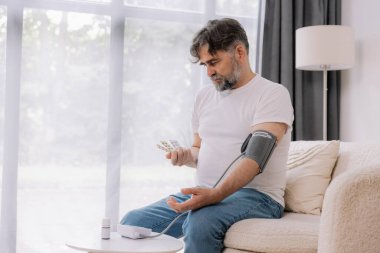 Evdeki kanepede oturmuş, tansiyonunu ölçen, gri saçlı, son sınıf öğrencisi. Modern tonometre kullanan emekli, hipertansiyon deneyimi yaşayan, kopyalama alanı