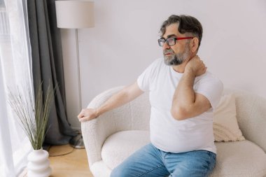 Üst sınıflardan biri içeride oturuyor, boynu ağrıyormuş gibi görünüyor. Üzüntülü bir ifadeyle boynunu tutuyor, rahatsız olduğunu gösteriyor..