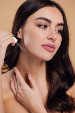 Bej arka planda Serum Bırakan Kadın. Pipette 'ten Serum Kolajeni Nemlendirici kullanan Avrupalı Kız. Yakın plan. Pozitif Gülen Güzel Kadın Portresi. Yüz Cildi Bakımı Konsepti