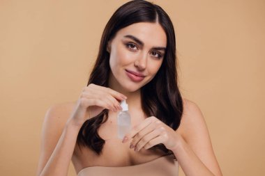 Bej arka planda Serum Bırakan Kadın. Pipette 'ten Serum Kolajeni Nemlendirici kullanan Avrupalı Kız. Yakın plan. Pozitif Gülen Güzel Kadın Portresi. Yüz Cildi Bakımı Konsepti