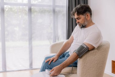 Evdeki kanepede oturmuş, tansiyonunu ölçen, gri saçlı, son sınıf öğrencisi. Modern tonometre kullanan emekli, hipertansiyon deneyimi yaşayan, kopyalama alanı