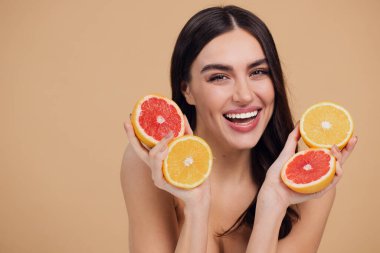 Genç bir kadının portresi, portakal rengi greyfurt gülümseyen dişlerin yarısını beslenen vejetaryen vitamin yaz vitamini, saç bakımı, doğal organik vegan narenciye bej arka planda.