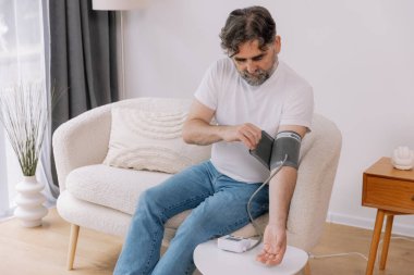 Evdeki kanepede oturmuş, tansiyonunu ölçen, gri saçlı, son sınıf öğrencisi. Modern tonometre kullanan emekli, hipertansiyon deneyimi yaşayan, kopyalama alanı