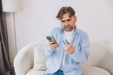 Yaşlı bir adam kanepede tek başına oturuyor. Bir hasta gözlük takıyor. Akıllı telefondan talimatları okuyor.