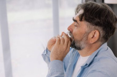 Evde burun spreyi kullanarak grip ve soğuk algınlığı geçiren yaşlı, olgun, hasta bir adam. rhinitis, ilaç ve sağlık hizmeti kavramı
