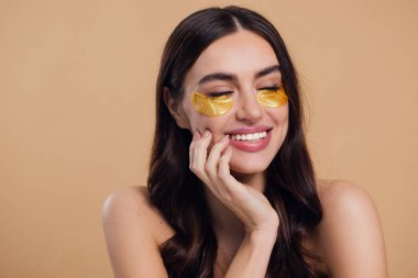 Saf, güzel, kibar bir kadının güzel görüntüsü. Çıplak, soyutlanmış bir kamera gibi duruyor. Bej arka planda altın rengi bantlarla cildine dikkat et.