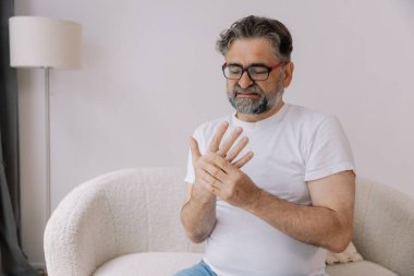Artrit belirtileri. Gözlüklü yaşlı adam evde acı çekiyor.