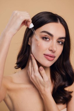 Bej arka planda Serum Bırakan Kadın. Pipette 'ten Serum Kolajeni Nemlendirici kullanan Avrupalı Kız. Yakın plan. Pozitif Gülen Güzel Kadın Portresi. Yüz Cildi Bakımı Konsepti