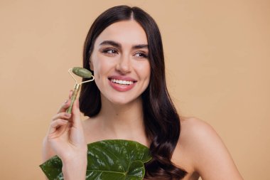 Mükemmel ciltli güzel bir kadının yarı çıplak portresini kapat. Bej arka planda doğal kuvars taşıyla yüz masajı yap..