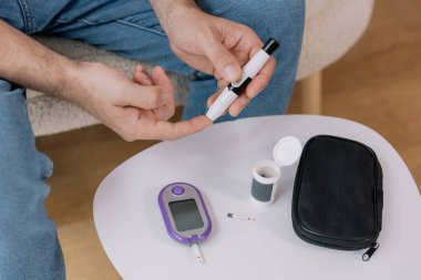 Tekerlekli sandalyedeki diyabetik kıdemli adam kan şekeri seviyesini parmak ölçer, glikoz ölçer. Tip 1 diyabeti olan yaşlı bir adam evde kan şekeri monitörü kullanıyor..