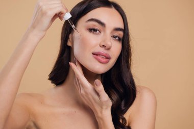 Bej arka planda Serum Bırakan Kadın. Pipette 'ten Serum Kolajeni Nemlendirici kullanan Avrupalı Kız. Yakın plan. Pozitif Gülen Güzel Kadın Portresi. Yüz Cildi Bakımı Konsepti
